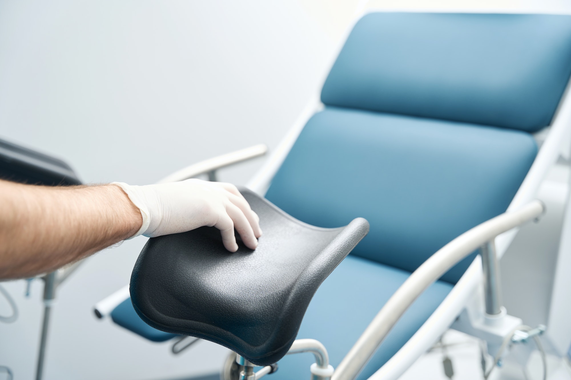 Gynecologist hand is touching the gynecological chair in the office